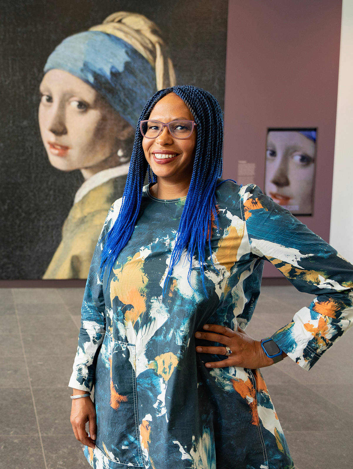 Portret van restaurator Abbie in de foyer van het Mauritshuis, op de achtergrond zie je een grote versie van het Meisje met de Parel.